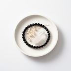 Black Obsidian bracelet flat lay on ceramic tray with crystals and dried flowers — editorial product photography