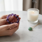 Manifestation Crystal Gift Set - hand holding Amethyst bracelet with candle and pendant on white marble
