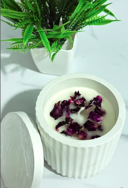 White ribbed ceramic jar candle with dried purple rose petals on white wax, lid beside it — real product photo