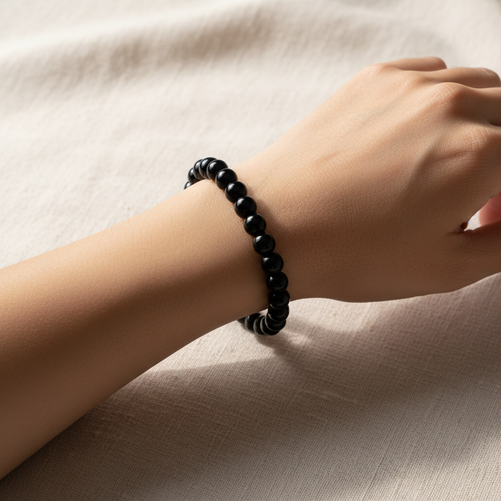 Close-up wrist shot of Black Obsidian bead bracelet on cream linen — wellness crystal jewellery