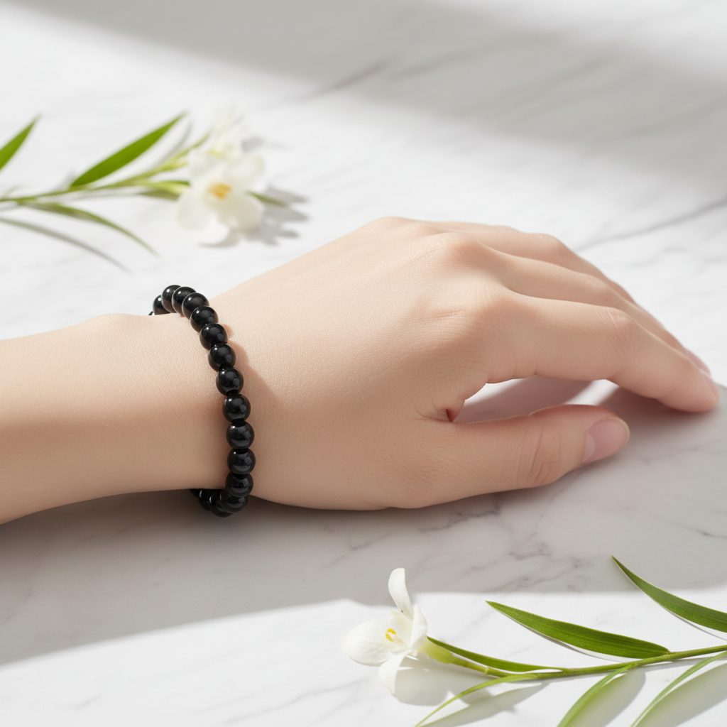 Hand wearing Black Obsidian bracelet on white marble with soft white flowers — luxury crystal bracelet