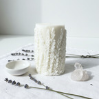 White botanical leaf relief pillar candle flat lay on white linen with dried lavender and crystal cluster
